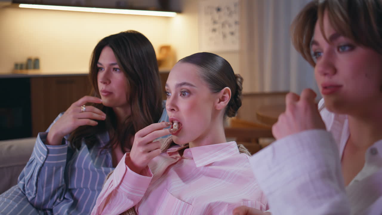 Emotional women watching film eating popcorn at couch closeup. Focused girls