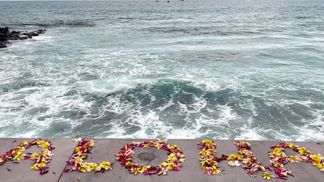 aloha spelled out in colorful flower petals welcoming guests as the lookout over waves crashing into the hawaiian beach