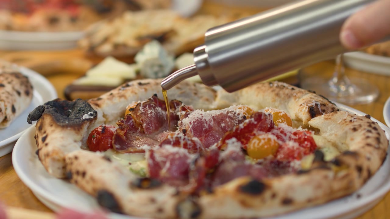 Primo piano di olio d'oliva versato a filo su una pizza gourmet con prosciutto e formaggio