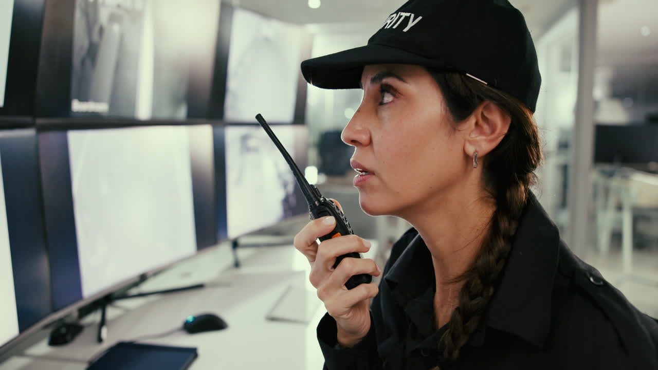 A security guard woman in uniform is monitoring security cameras while talking on radio