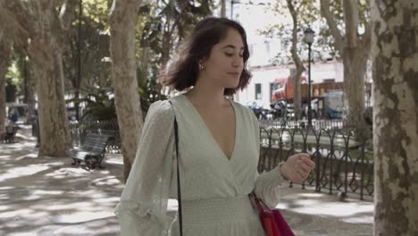 mujer joven latina sosteniendo bolsas en el codo y caminando por la calle