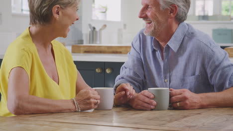 Küssendes-Rentnerehepaar,-Das-Zu-Hause-Am-Tisch-Sitzt-Und-Gemeinsam-Morgenkaffee-Trinkt