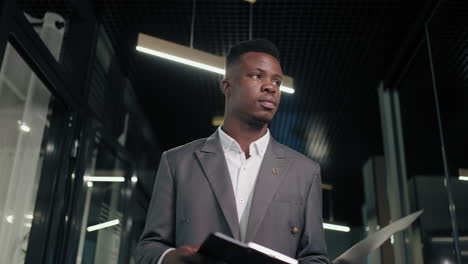 Portrait-of-focused-businessman-walking-on-meeting-in-office-corridor.-african-american-man-walking-in-corridor.-Serious-afro-business-man-going-with-folder-in-business-center-hallway.