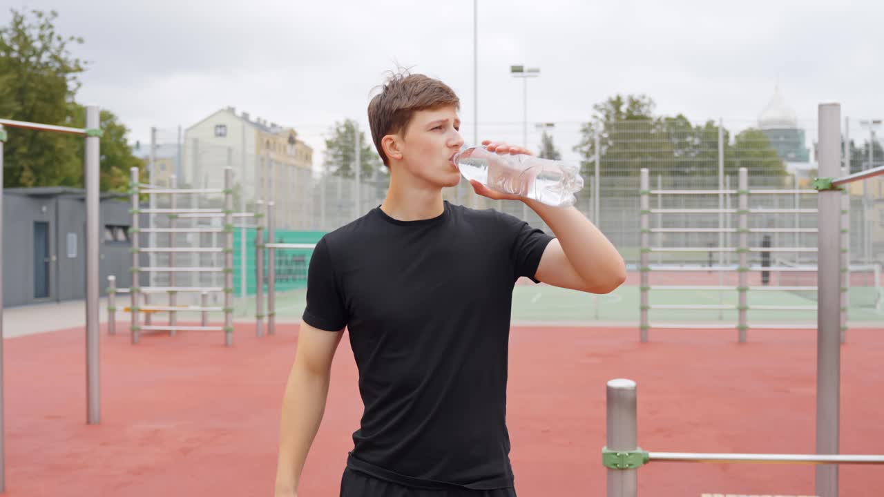 Fit young man drinking water from plastic bottle on outdoor street workout outdoor gym, fitness break, hydration, sport and healthy lifestyle