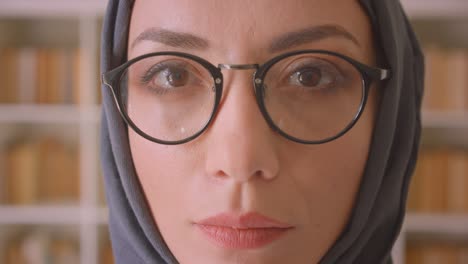 closeup portrait of young muslim female face in glasses and hijab looking at camera smiling happily in library indoors