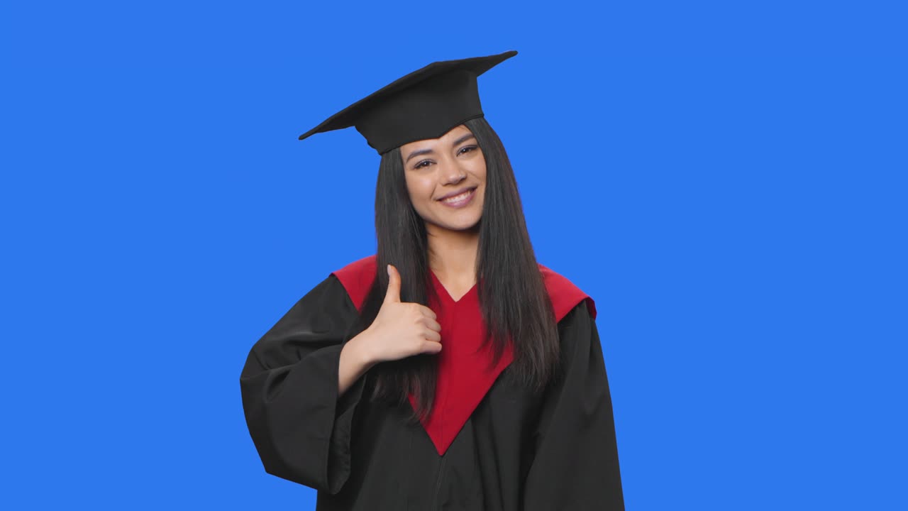 Portrait of female student in graduation costume pointing side hand for something then nods and shows thumb like. Young woman posing on blue screen background. Close up. Slow motion ready 59.94fps