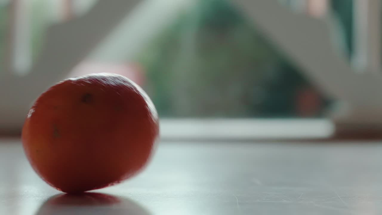 오렌지색 클레멘타인 한 개가 배경에 창문이 있는 테이블에 떨어졌습니다.