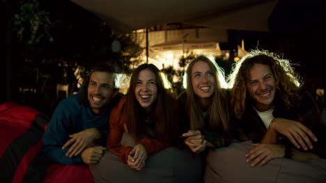 Close-up-shooting:-Two-couples-in-love-lie-on-beanbag-chairs-and-watch-a-movie.-A-party-outside-the-city.-Rest-in-the-country-house