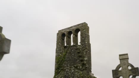 Moss-lichen-covered-church-tower-and-arch-windows-with-eerie-old-graveyard-headstones