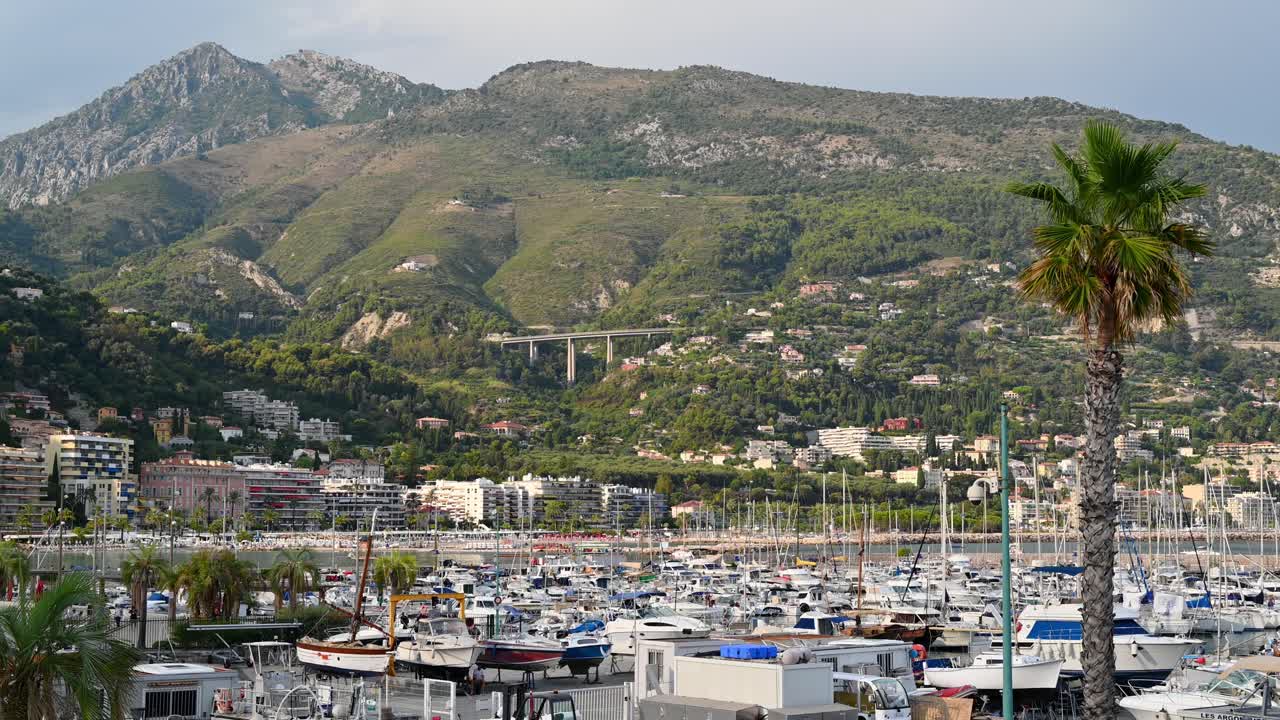 View of the sea port in Menton, France. Moored boats and yachts, hills covered with greenery and buildings on the background
