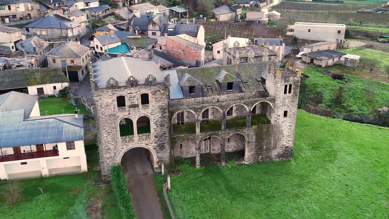Aerial photograph of an ancient stone castle with arched windows and towers, surrounded by greenery and a rural village in Valdeorras.