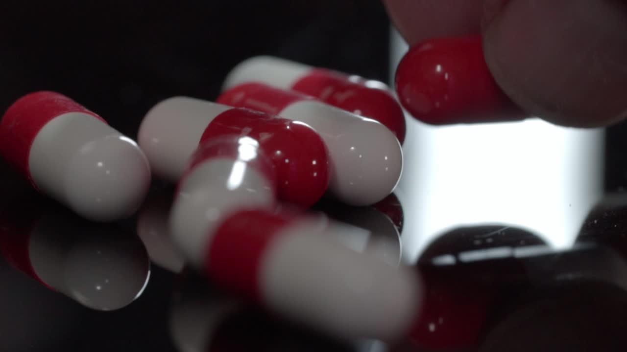 Close up of human hand picking red and white pharmaceutical capsule on reflective black surface