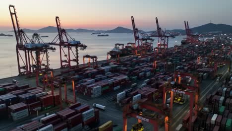 aerial view of a busy shipping port at dusk with container stacks, cranes, and ships in the harbor, showcasing maritime cargo operations and logistics