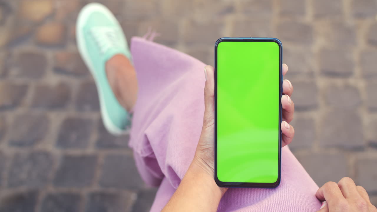 Persona che tiene in mano uno smartphone con schermo verde all'aperto