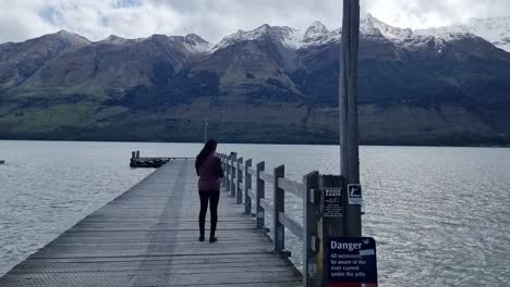 Mujer-De-Pie-En-El-Embarcadero-De-Glenorchy-Con-Las-Montañas-Cubiertas-De-Nieve-En-El-Fondo