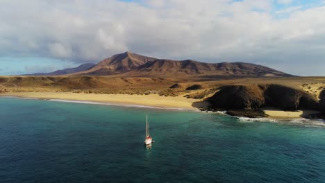 lonely sailboat near majestic coastline of lanzarote with mountain in background, aerial view