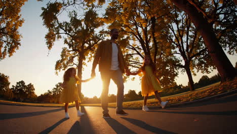 father and daughters walking hand-in-hand in a park at sunset