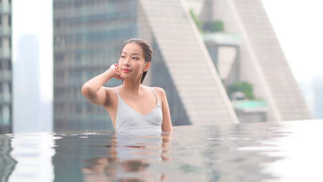 옥상 수영장에 있는 한 여성이 손을 뻗어 얼굴에서 머리카락을 빗질합니다.