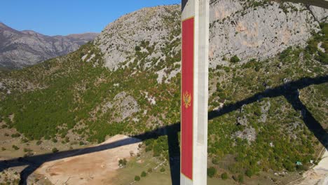 aerial shot of the fully finished moracica bridge in montenegro. the big red coat of arms of montenegro is seen on one of the bridge's pillar