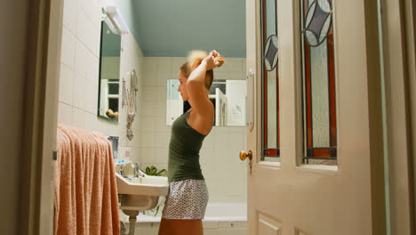 woman tying her hair in bathroom at home 4k