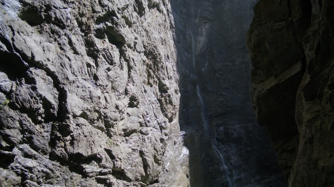 la luz del sol golpeando las rocas con una cascada que fluye en la distancia | grindelwald suiza cueva en el cañón del glaciar, europa, 4k
