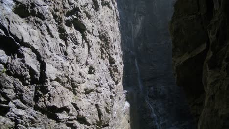 Sunlight-Hitting-Rocks-With-Flowing-Waterfall-In-Distance-|-Grindelwald-Switzerland-Cave-in-Glacier-Canyon,-Europe,-4k