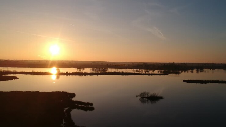 Tomada aérea panorâmica de pôr do sol em hora dourada com reflexo do céu azul-petróleo e laranja