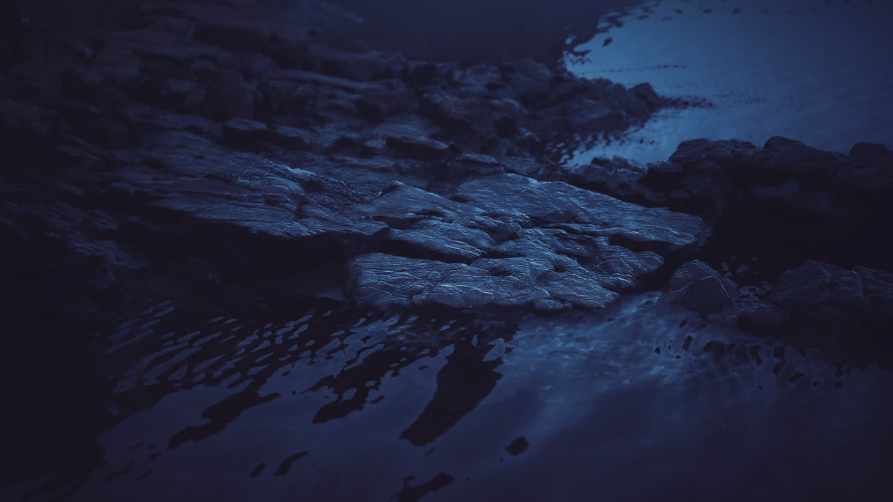 Misty water surface reflecting stones at twilight near a tranquil shoreline