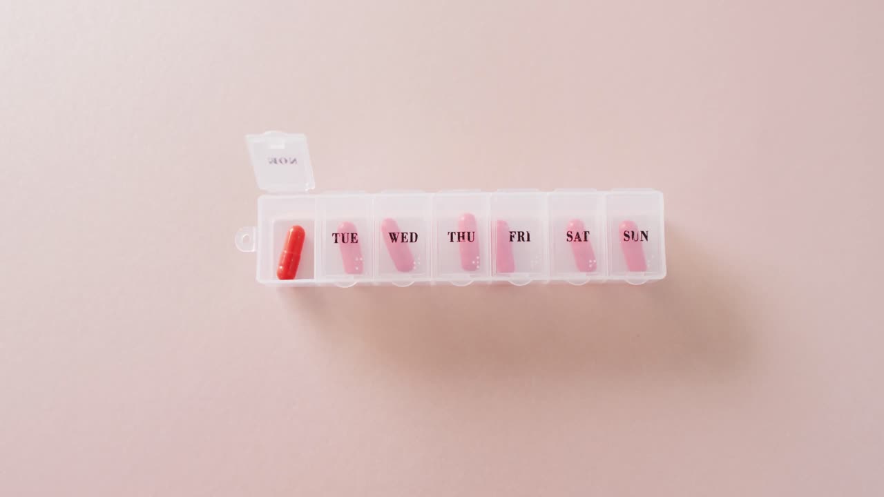 Video of red pills in weekly pill box on pink background with copy space