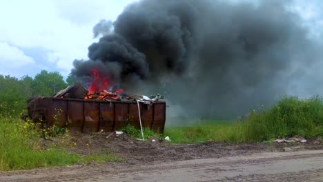 thick dark smoke billowing from a burning dumpster full of garbage on rural farmland