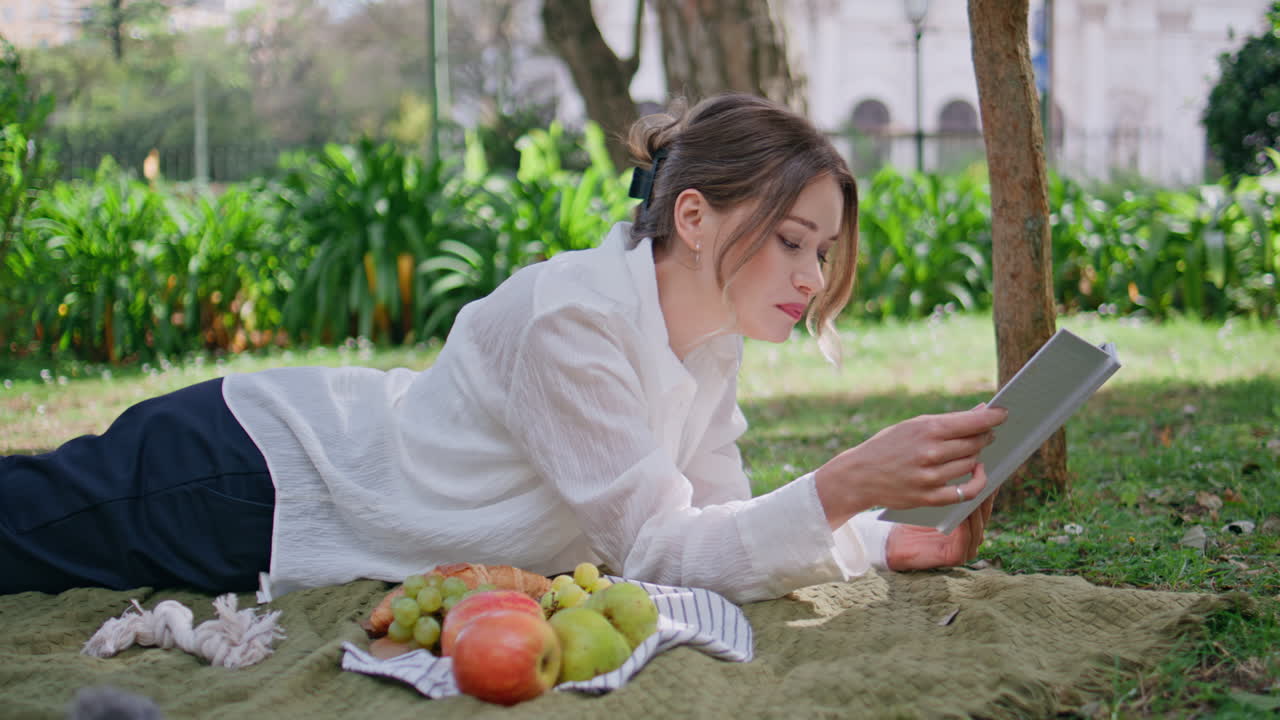 Reading girl lying blanket at green grass park eating apple closeup. Happy woman