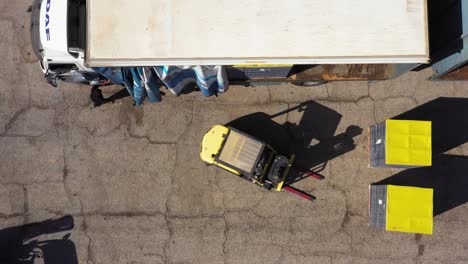 forklift loading product pallets into shipping truck, bird's eye view