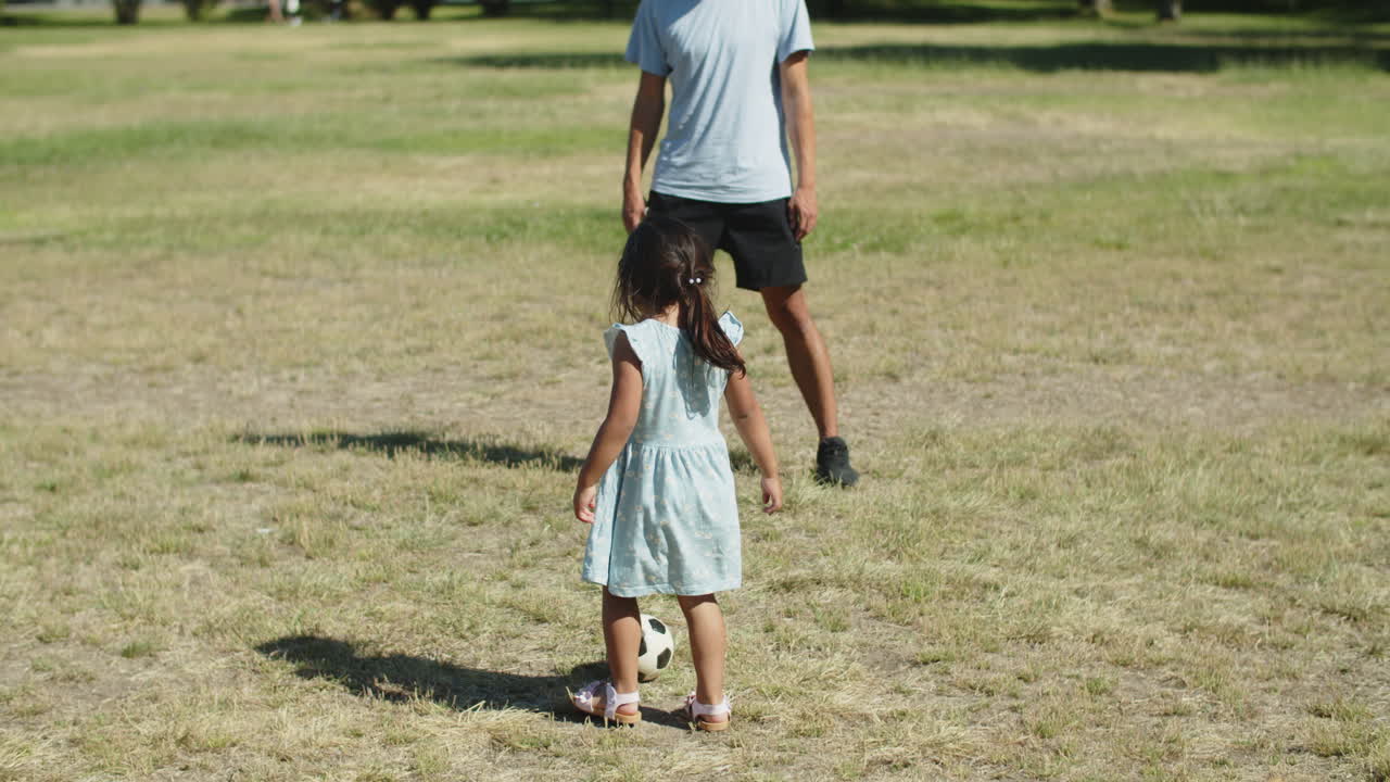 niña asiática feliz jugando a la pelota con su padre en el parque