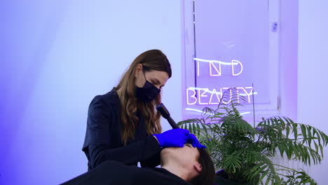 caucasian brunette female lies on the couch in beauty salon. beautician carrying out the procedure of permanent make up for eyebrows.
