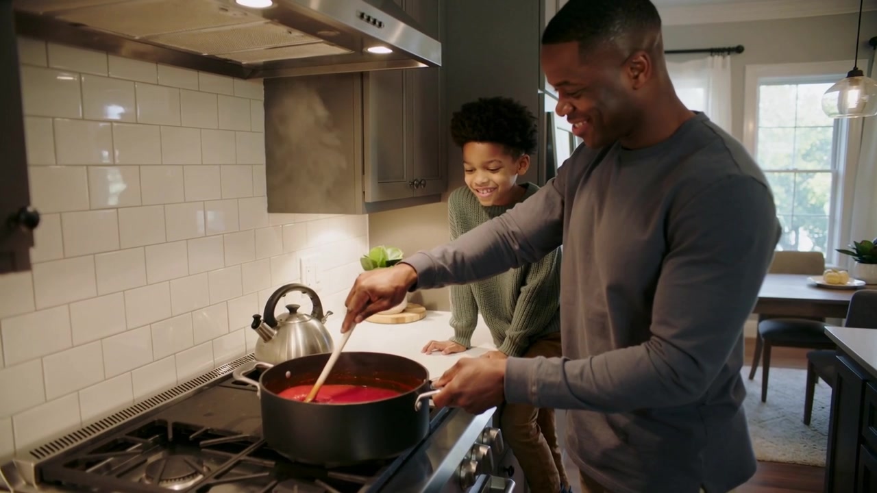 Stirring father and son monitoring sauce heating for dinner at home, wooden spoon, pot, copy space