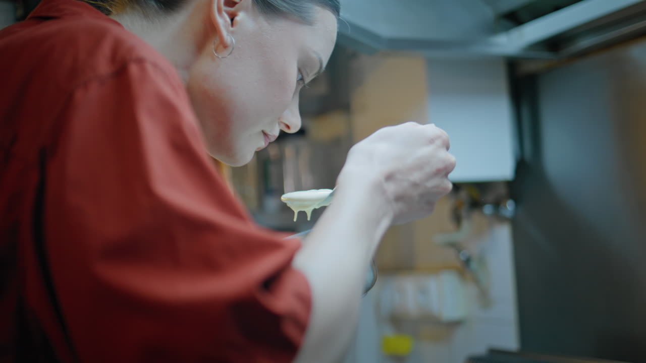 Professional woman sniffing sauce in spoon cooking food at kitchen closeup