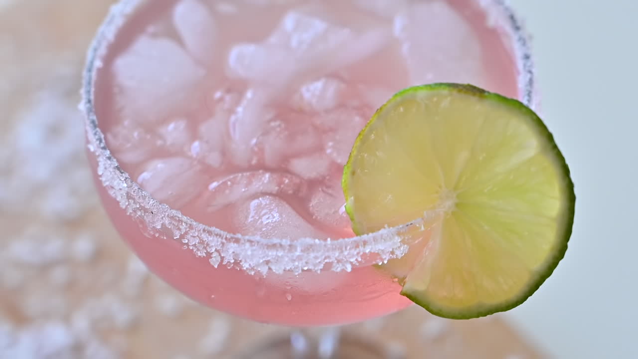 Primer plano de un cóctel rosa claro con hielo y rodajas de lima