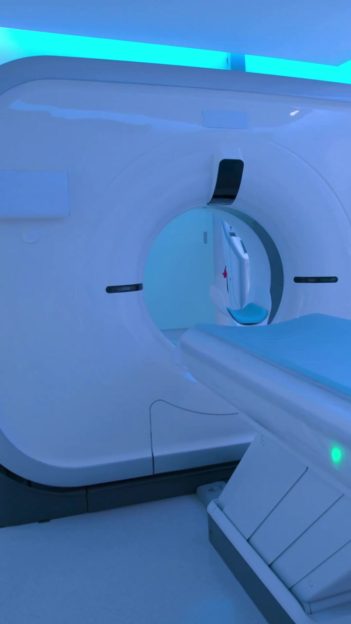 Video verticale: Telecamera in movimento che mostra il tavolo che entra nel gantry della TAC in sala d'esame, con un cuscinetto blu e un serbatoio.