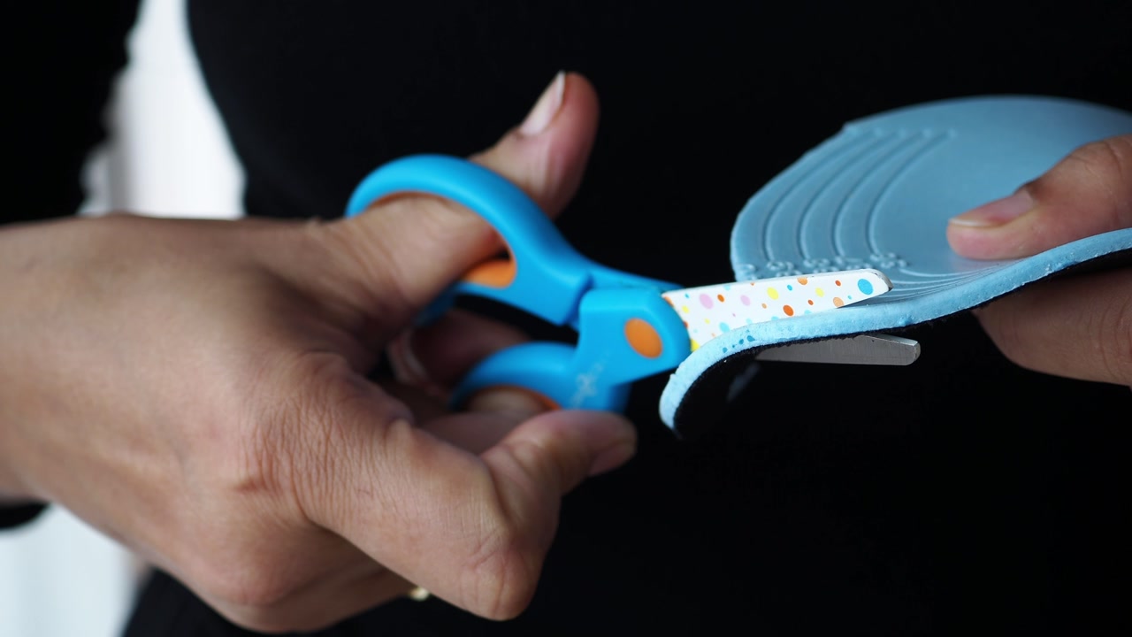 Close-Up of Hands Cutting Blue Foam Material with Scissors