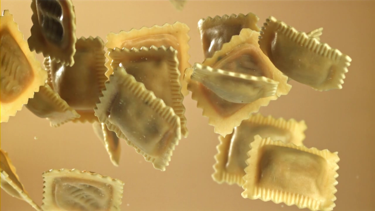 ベージュの背景をバックにスローモーションで落ちる未調理のラビオリパスタ