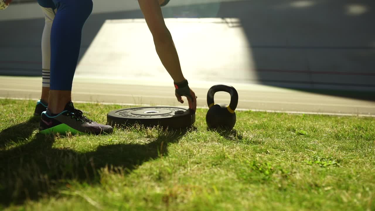 잔디 에서 야외 에서 케틀벨 과 웨이트 플레이트 를 사용 하여 운동 하는 사람