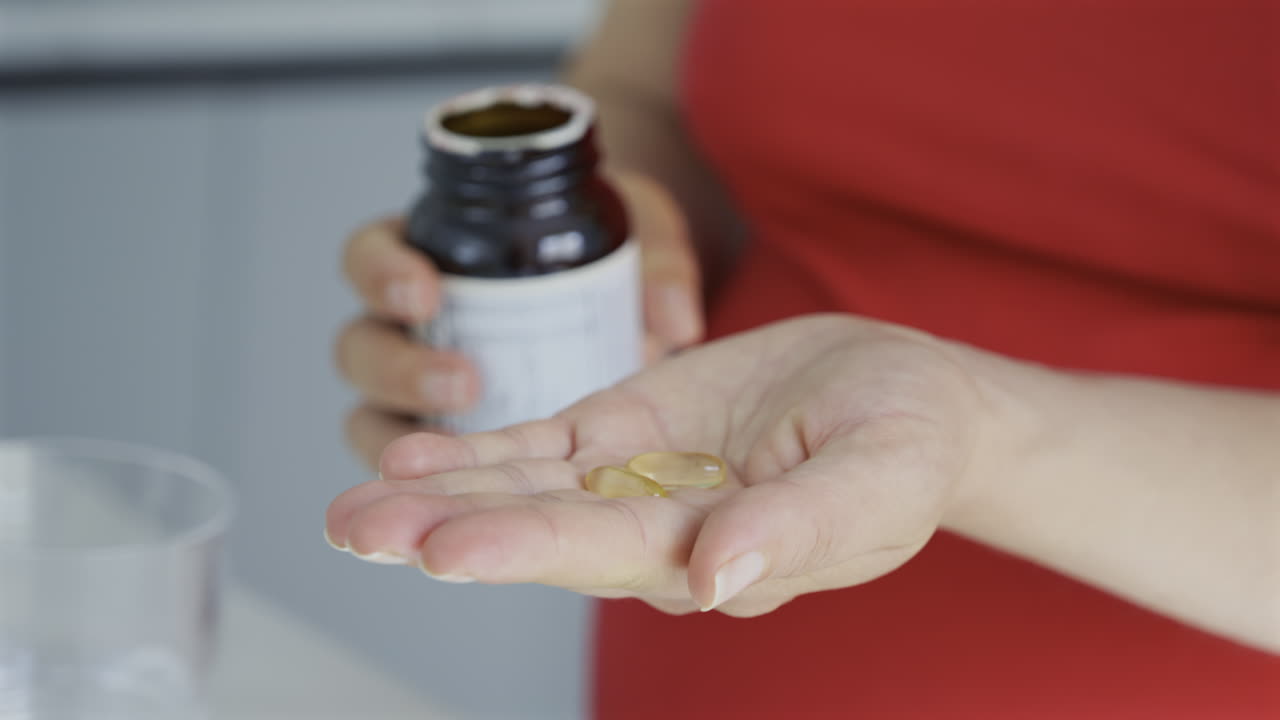 Close up of a pregnant woman pouring fish oil supplements out of into her palm