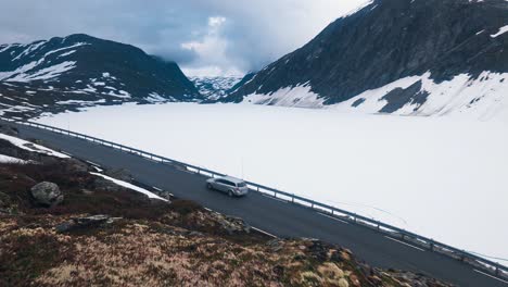 car driving on a road through the mountains, surrounded by snow and a blue sky