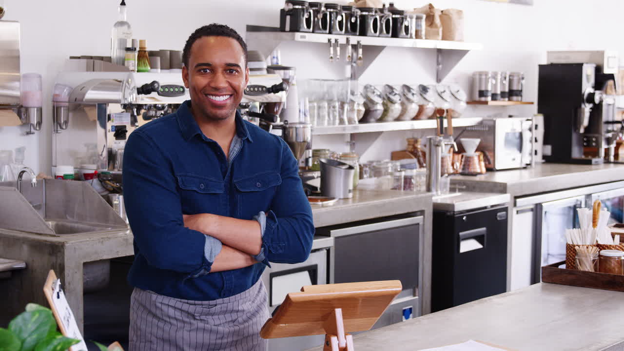 Young black male coffee shop owner smiling behind counter