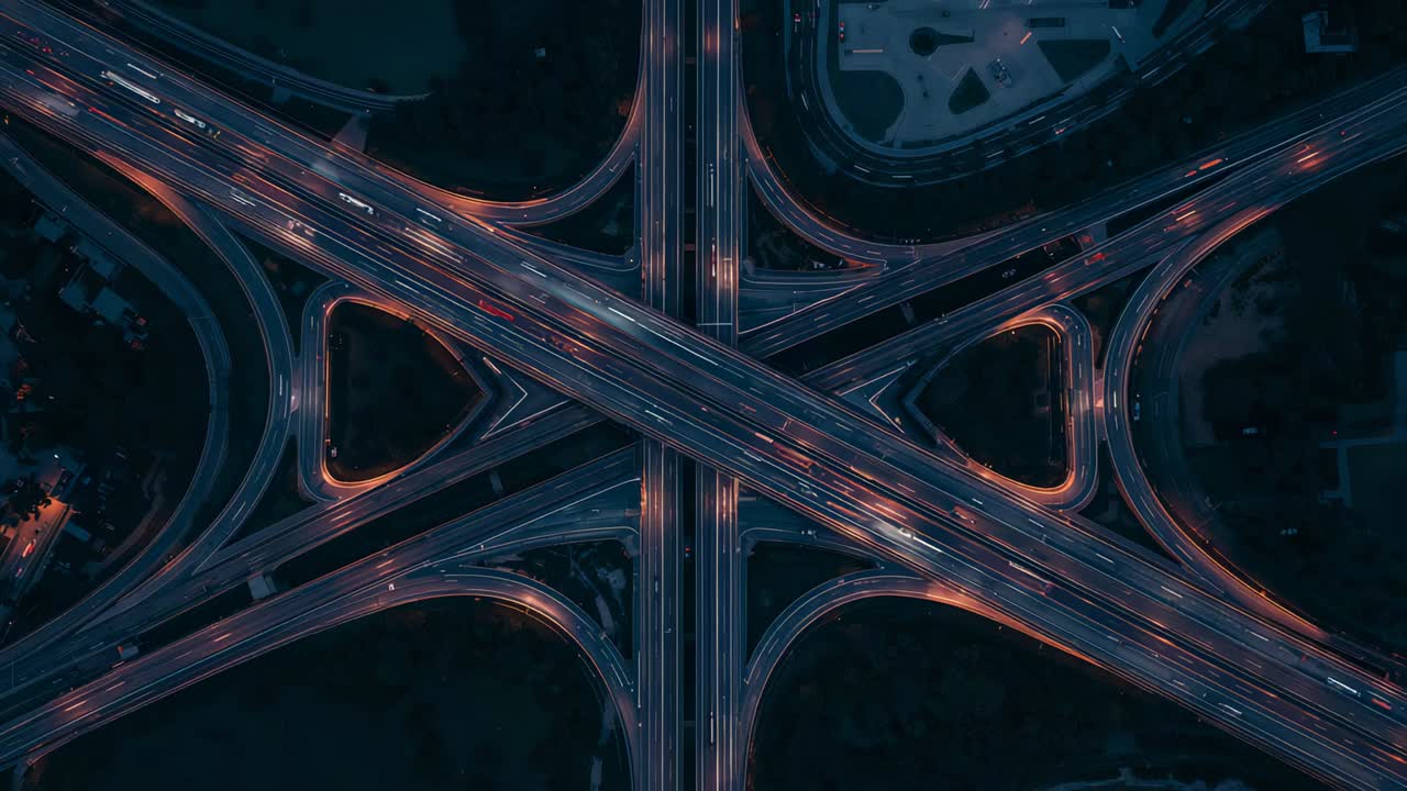Streaming vehicles merging and advancing on interchange ramps at dusk, maintaining steady flow