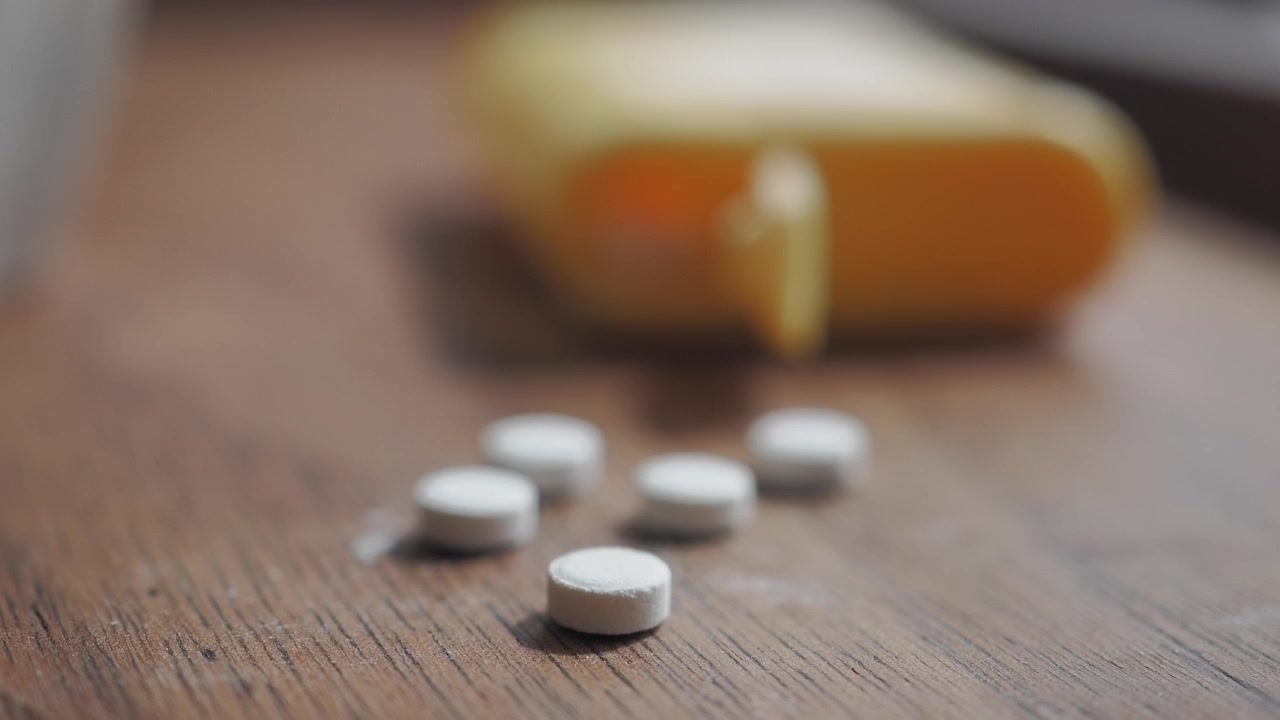 White Pills Scattered on Wooden Table with Yellow Container