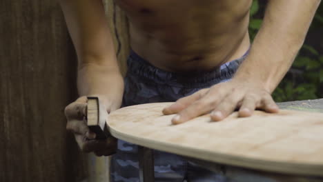 trabajador frotando papel de lija para alisar los bordes y dar acabado de madera a la nueva patineta