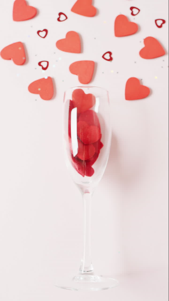 вертикальное видео шампанского стакана с красными формами сердца на белом фоне