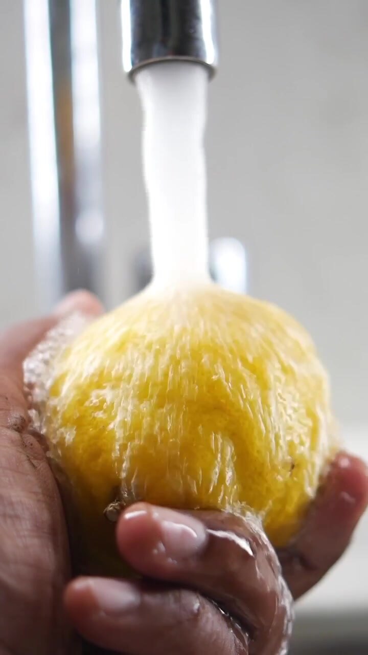 Person Washing a Fresh Yellow Lemon Under Running Water