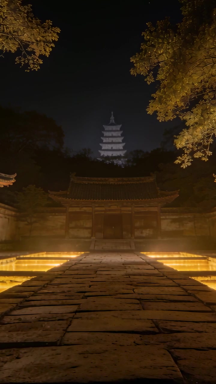 Video vertical: Cámara moviéndose lentamente por un sendero de piedra hacia la puerta de un templo de noche, revelando una pagoda